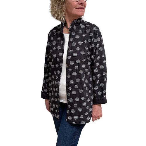 Woman wearing a black patterned shirt over a white top with blue jeans on a white background