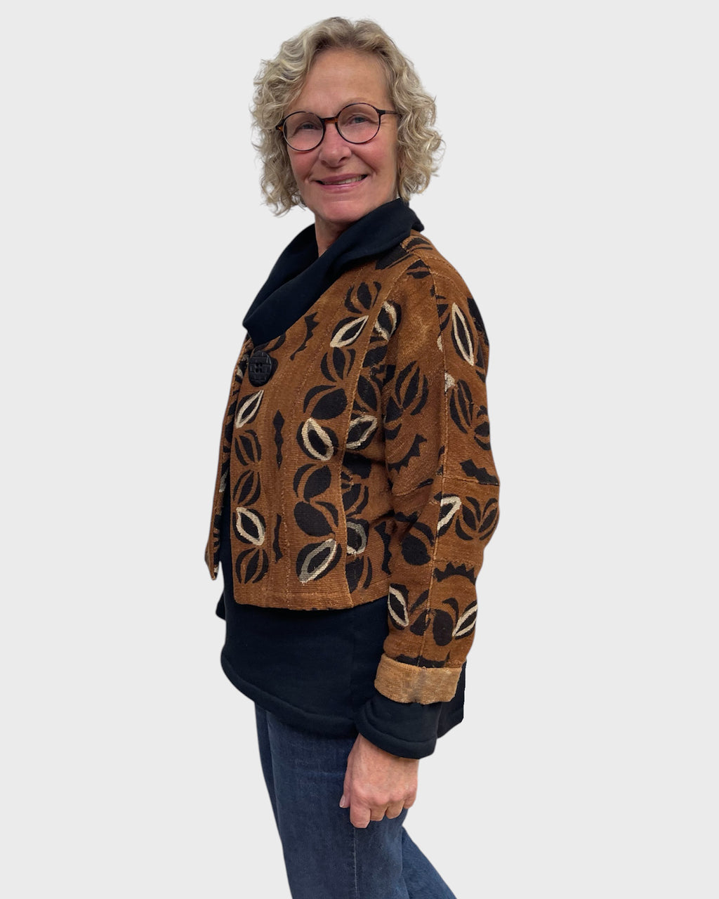 Side view of short rust mudcloth bolero jacket with black and cream leaf pattern and turned back cuffs