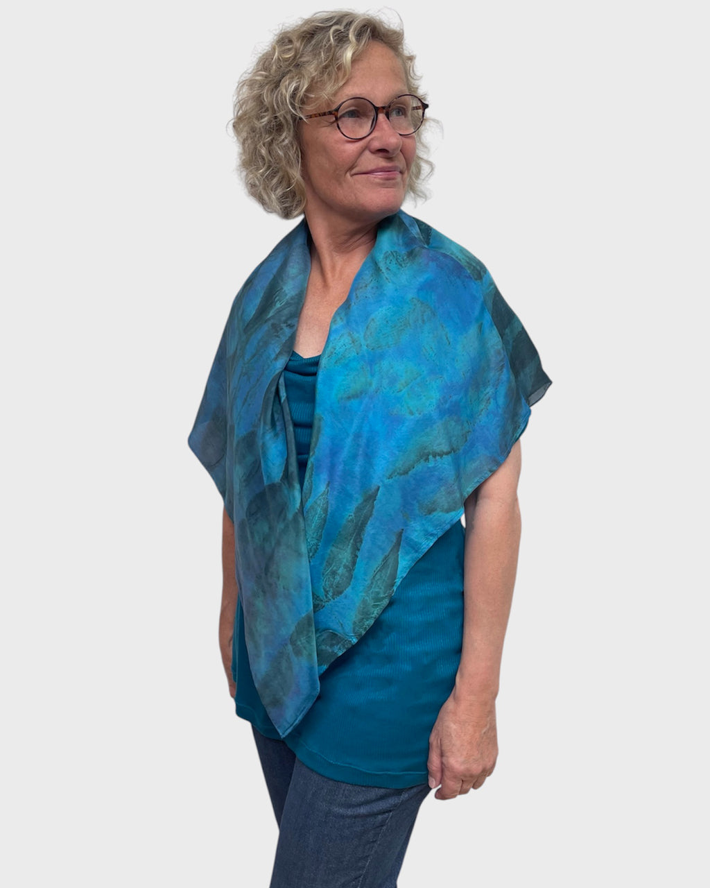 Woman wearing turquoise silk poncho with black walnut eco print, V-neck draped open, side view
