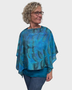 Model wearing turquoise silk poncho with boat neck styling, black walnut leaf print detail visible