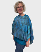Woman wearing turquoise silk poncho with boat neck styling, front and center view