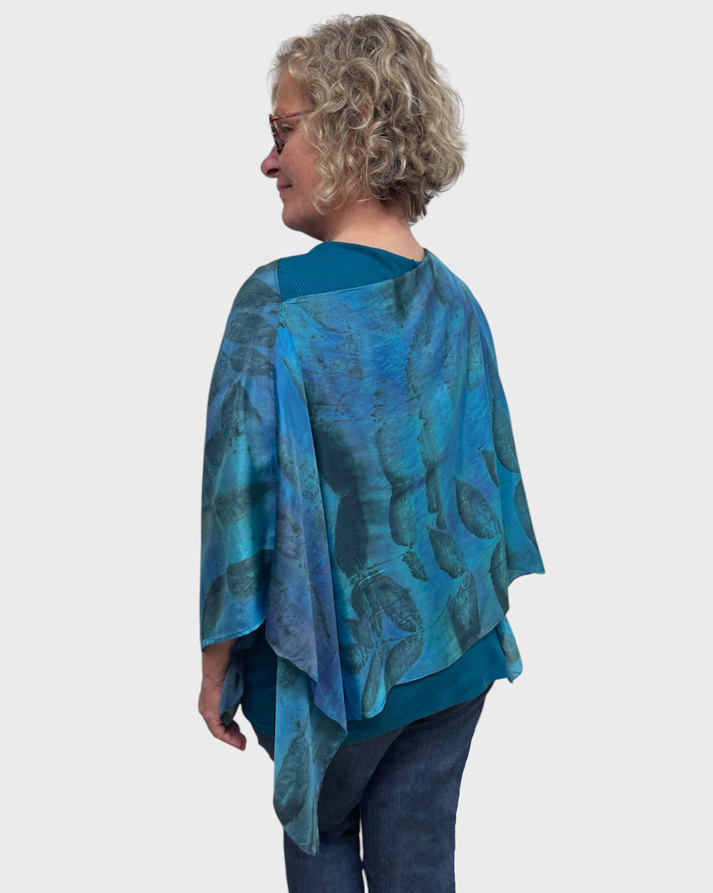 Back three quarter view of turquoise eco print silk poncho, leaf pattern draping over shoulder