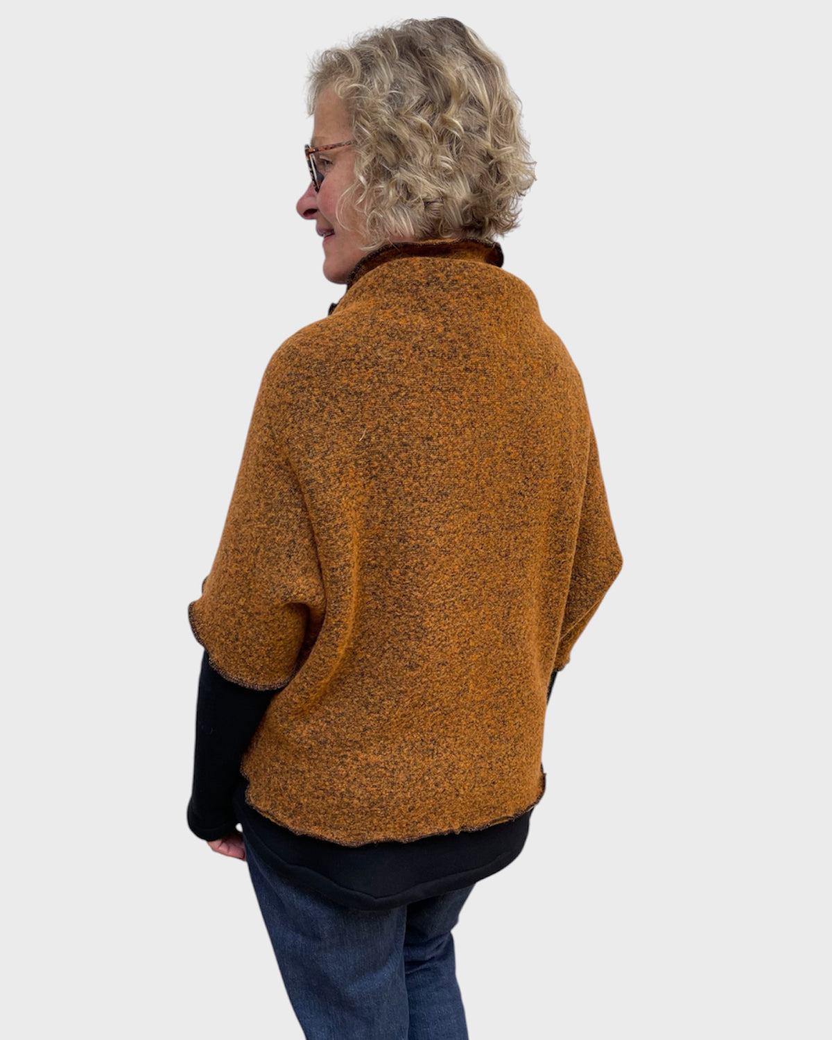 Back side view of a cozy pumpkin and black stretch shrug over a black top and jeans